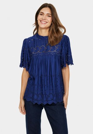 Blusa blu Navy con maniche a palloncino corte, intricato ricamo ad occhiello, corpetto arricciato e orlo ondulato. Tessuto morbido e leggero.