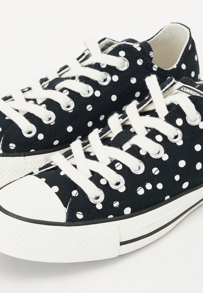 Zapatillas de lona negras con lunares blancos, cordones blancos y puntera de goma. Presentan ojales plateados y suelas de goma negra.