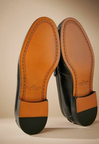Zwarte leren schoenen met bruine lederen zolen, voorzien van een gestikt ontwerp en textuurelementen bij de hak. De afwerkingsdetails zijn zichtbaar.