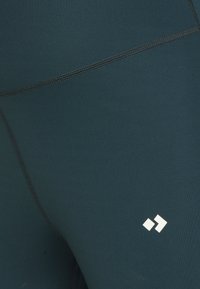 Legíny v tyrkysové barvě z elastické tkaniny s žebrovanou strukturou. Obsahují kontrastní bílý detail loga a ploché švy pro pohodlí.