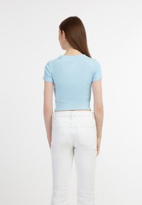 Világoskék bordázott rövid ujjú cropped top, kerek nyakkivágással, fehér, testhezálló farmernadrággal párosítva. A top szorosan illeszkedik és sima tapintású.