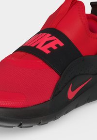 Κόκκινο και μαύρο αθλητικό παπούτσι Nike slip-on με φαρδιά λωρίδα πάνω από το πάνω μέρος με το λογότυπο της Nike σε κόκκινο χρώμα σε μαύρο φόντο.