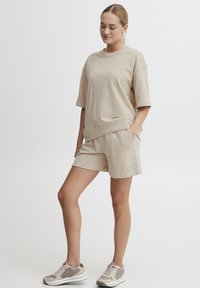 Sweatshirt en coton beige à manches courtes, associé à un short assorti avec poches. La tenue est complétée par des baskets grises et blanches.