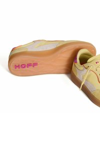 Zapatillas bajas con parte superior de ante amarillo, acentos rosas y suela de goma con patrón que presenta el logo "HOFF" en el talón.