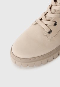 Botín de cuero beige hasta el tobillo con punta redonda, cierre de cordones en la parte delantera y suela de goma texturizada que presenta un patrón de tracción.