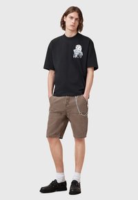Black cotton t-shirt with graphic design, beige shorts with pockets and chain detail, and black lace-up shoes with white socks.