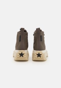 Baskets montantes marron en cuir texturé, avec une semelle crème contrastante et un accent étoile noir sur le talon. Détail de marque subtil.