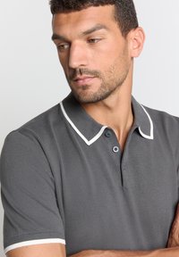 Grijze polo-shirt met witte accenten op de kraag en mouwranden, met een geribbelde textuur en een drieknopssluiting.