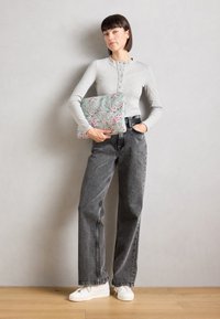 Grå langærmet skjorte med knapdetaljer, høj talje sorte jeans og hvide sneakers. Holder en mintgrøn taske med blomsterprint.
