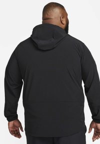 Zwarte capuchonjas met een gladde textuur, voorzien van lange mouwen, een losse pasvorm en een eenvoudig ontwerp zonder extra patronen of accenten.