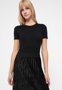 Zwarte geribbelde top met korte mouwen en een aansluitend ontwerp, gecombineerd met een zwarte plooirok met een gestructureerde afwerking en subtiele glans.