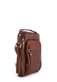 Brązowa skórzana torba na ramię z przednią kieszenią na zamek, regulowanym paskiem i mosiężnymi elementami na białym tle.