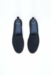 Chaussures slip-on en velours noir avec une semelle intermédiaire en jute tressé et des détails de couture contrastants. L'intérieur présente une doublure douce et lisse. Nom de la marque inclus.