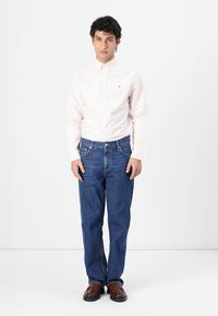 Lichtroze langblijvende overhemd met knopen, blauwe denim jeans en bruine leren schoenen. Effen stof zonder zichtbare patronen of accenten.