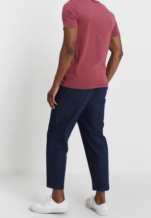 Bordowa koszulka z krótkim rękawem połączona z granatowymi, krótkimi spodniami o luźnym kroju oraz białe trampki. Gładka tkanina bez wzorów.