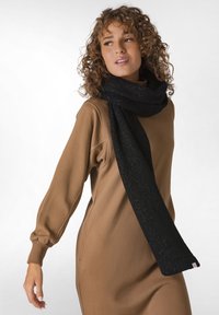 En sort strikket tørklæde med en diskret glimmer hænger afslappet om halsen og er parret med en beige langærmet kjole med en løs pasform.