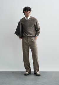 Brun stickad tröja med V-ringning, kombinerad med texturerade bruna byxor. Accessoarer inkluderar en svart tote-väska och beige skor.