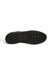 Semelle de chaussure en caoutchouc noir avec un motif de crantage texturé, présentant des grips prononcés et une zone centrale lisse pour la stabilité.