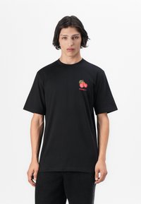 T-shirt noir à manches courtes en coton. Présente un petit graphique de cerise rouge et un logo "adidas" sur la poitrine gauche. Design avec une coupe droite.