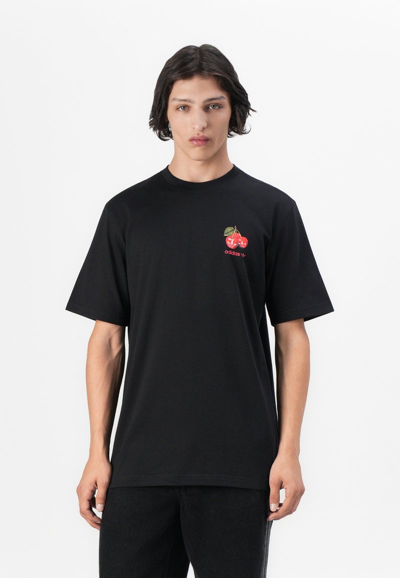 T-shirt noir à manches courtes en coton. Présente un petit graphique de cerise rouge et un logo "adidas" sur la poitrine gauche. Design avec une coupe droite.