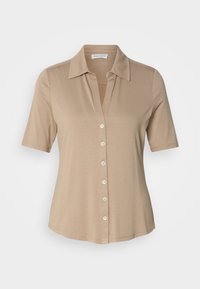 Chemise beige à manches courtes avec col, fermeture à boutons à l'avant et texture lisse. Comporte six boutons et une coupe légèrement ample.