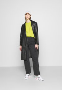 Cappotto di pelle nero, camicia verde lime brillante, pantaloni cargo neri, sneaker grigie e bianche, e un cappellino bianco. Elementi di design semplici e moderni.
