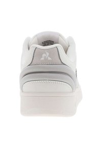 Basket blanche avec une tige en cuir lisse et des accents en textile gris, dotée d'un col rembourré et d'une semelle texturée. Détail du logo au talon.