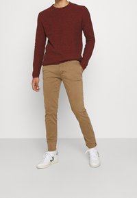 Rode textuurtrui, kaki chino's en witte sneakers met groene accenten. Strak aanstaand met een ronde halslijn en een taps toelopend ontwerp.