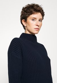 Maglione lavorato a maglia blu navy, con collo alto a mock, texture a coste, vestibilità ampia, caratterizzato da un design semplice e un tessuto morbido.