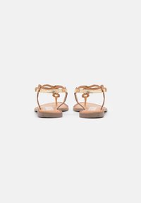 Sandalias planas marrones con tiras doradas, diseño con ondas y una plantilla texturizada. Presentan una hebilla ajustable en el tobillo para un ajuste seguro.