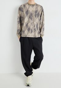 Langärmliger, grauer Sweatshirt mit diamantförmigem Muster, Rundhalsausschnitt und gerippten Bündchen, kombiniert mit locker sitzenden schwarzen Hosen und hellen Sneakern.