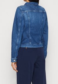 Giacca in denim blu scuro con colletto, polsini con bottoni e tasche laterali. Presenta un design aderente e dettagli di cucitura in evidenza.