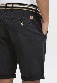 Pantaloni corti neri realizzati in tessuto misto cotone. Presentano un risvolto, una patch in pelle del marchio e una cintura a strisce contrastanti.