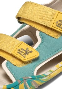 Turquoise and yellow sandal with two adjustable straps, suede material, and a cartoon dog-shaped accent on the strap. Features open design.