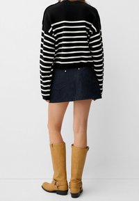 Pull à rayures noires et blanches, jupe en denim foncé et bottes hautes couleur cognac avec détail boucle. Mise en valeur du design ajusté et des textures superposées.