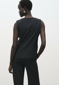 Top negro sin mangas con corte recto, textura suave y ligero corte en la parte posterior, combinado con pantalones de pierna ancha oscuros a juego.