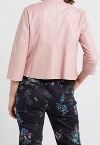 Rosa lädercroppad jacka med trekvartsärmar och sömdetaljer, tillsammans med mörka byxor med blommönster och färgglada accenter.