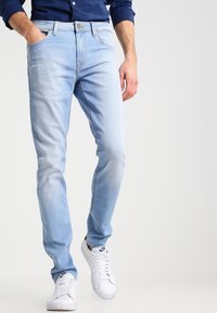 Jeans de mezclilla azul claro con corte ajustado, que presentan bolsillos delanteros y zonas desgastadas. Combinados con zapatillas blancas.