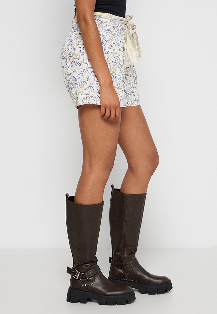 Blumen-Shorts aus leichtem Stoff mit gebundenem Bund, kombiniert mit schokoladenbraunen knielangen Stiefeln mit Schnallenakzenten und robusten Sohlen.