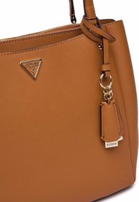 Borsa a tracolla in finta pelle marrone con un design strutturato. Presenta un logo triangolare, chiusura con zip e un'etichetta staccabile con "GUESS."