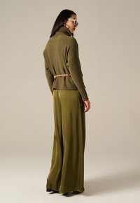 Maglione a maglia verde oliva con colletto alto e maniche a coste, abbinato a pantaloni a gamba larga coordinati. Accentuato da una sottile cintura beige.