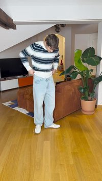 Jeans de mezclilla azul claro con un corte holgado, combinados con un suéter a rayas blancas y negras. El entorno presenta un sofá marrón y una planta.