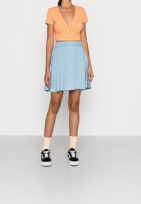Oranges Kurzarm-Crop-Top mit weißem Blumenmuster, kombiniert mit einem hellblauen ausgestellten Jeansrock und schwarzen Sneakers mit weißen Akzenten.