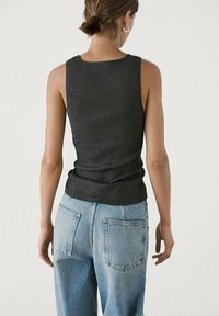 Canotta a coste grigia scura con una silhouette aderente, abbinata a jeans a vita alta blu chiaro con tasche posteriori.
