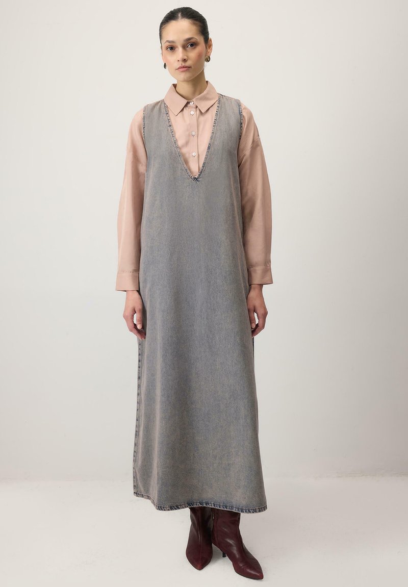 Világosszürke farmerruha maxi hosszban, V-nyakkivágással, kontrasztos varrással. Egy pasztell rózsaszín inget viselnek alatta, és bordó csizmával párosítva.