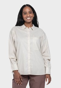 Light beige button-up shirt with long sleeves, collared design, a single chest pocket, and a subtle triangle logo on the pocket.