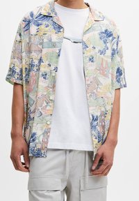 Koszula z krótkim rękawem w wielokolorowy, tropikalny wzór w pastelowych odcieniach, z zapięciem na guziki i luźnym krojem, zestawiona z białym t-shirtem.