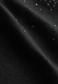 Țesătură neagră cu o țesătură texturată, având picături mici și reflectorizante, dispersate pentru un plus de detaliu.