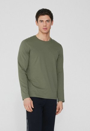 Langärmliges olivgrünes T-Shirt aus weicher Baumwolle, mit rundem Ausschnitt und körpernahem Schnitt, kombiniert mit dunklen Hosen.