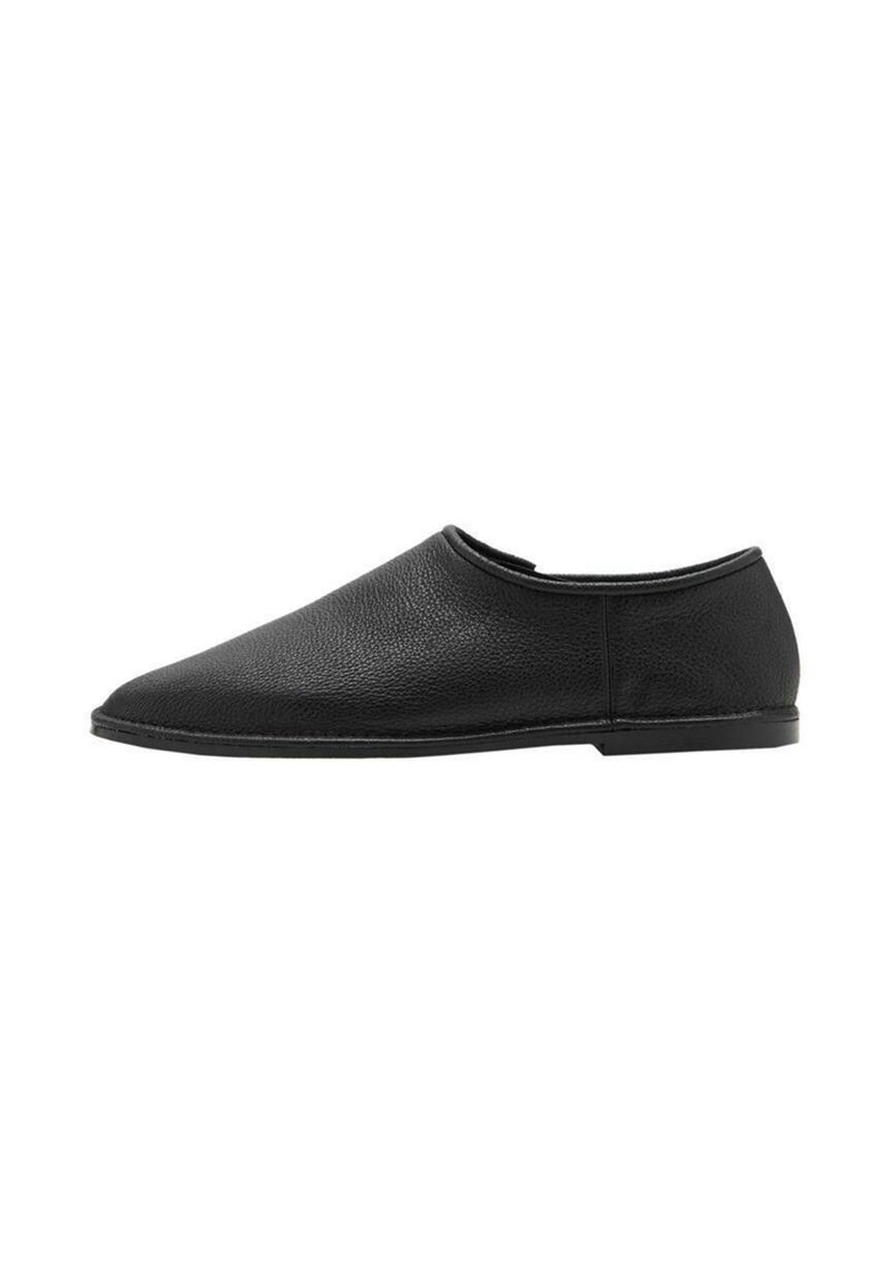 Zapato de piel negra tipo mocasín con punta redondeada y diseño minimalista. Presenta una textura suave y suela de goma de perfil bajo.
